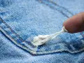 Finger versucht, Kaugummi aus Jeans zu entfernen. Der klebrige weiße Klumpen haftet an der blauen Denim-Oberfläche.
