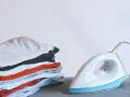 Ein Stapel bunter Kleidung neben einem weißen, easy home bügeleisen.