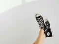 Beine mit schwarzen Chucks, die in der Luft baumeln. Zeit, die Lieblingsschuhe zu waschen!