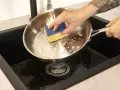 Hand reinigt mit einem Schwamm den schmutzigen Pfannenboden in der Spüle.
