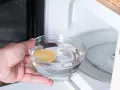 Hand placing a bowl of water with lemon slice into a microwave for cleaning.