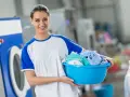 Lächelnde Frau mit Wäschekorb voller bunter Kleidung vor einer Waschmaschine. Sie weiß, wie man richtig waschen.