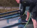 Mann reinigt mit Gartenschlauch das Glasdach von unten.
