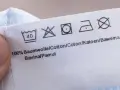 Pflegesymbol: Nicht im Trockner trocknen. Das Etikett zeigt auch Wasch- und Bügelsymbole für 100% Baumwolle.