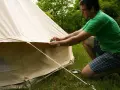 Mann reinigt mit einem Schwamm das beige Zelt. Er kniet auf dem Gras neben dem Zelt.