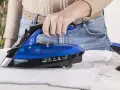 Eine Hand hält einen blauen, kabellosen Dampfbügeleisen über einem weißen Hemd.