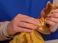 Hände polieren einen goldenen Kerzenständer mit einem gelben Tuch. Messing reinigen für neuen Glanz.