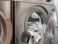 Waschmaschine mit offener Tür und grauen Handtüchern. Perfekt, um hartnäckige colaflecken entfernen zu lassen.