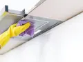 Gelbe Handschuhe wischen mit einem lila Tuch über die Dunstabzugshaube. Alu reinigen für strahlenden Glanz in der Küche.