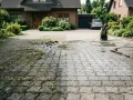 Hochdruckreiniger befreit Pflastersteine und Fugen von Moos und Schmutz. Vorher-Nachher-Effekt auf der Einfahrt vor einem Haus.
