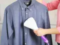 Dampfsteamer test: Eine Person glättet ein blaues Hemd mit einem Handdampfglätter.