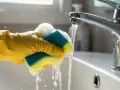 Gelbe Handschuhe reinigen mit einem nassen Schwamm das Waschbecken. Wasser spritzt.