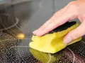 Hand reinigt mit Schwamm und Schaum das Ceranfeld.