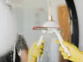 Gelbe Handschuhe und ein Wischer reinigen einen beschlagenen Spiegel.