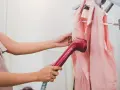 Eine Frau glättet mit einem Handdampfer ein rosa Kleidungsstück. Perfekt für die Vorbereitung auf die nächste steamer reise.