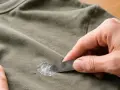 Mit einem Spachtel wird versucht, hartnäckiges Silikon aus Kleidung zu entfernen.