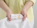 Hände halten ein weißes T-Shirt mit braunen, unbekannten Flecken nach dem Waschen.