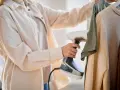 Frau testet Dampfbügler an Kleidung. Schnell und einfach Falten entfernen.