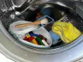 Bunte Lego-Steine in einem Wäschenetz, ein Spielzeugauto und ein gelbes Tuch in einer Waschmaschinentrommel.
