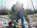 Kind spielt mit Spielzeugtraktoren im Matsch. Die Kleidung wird wohl bald eine Wäsche brauchen, um die matschflecken entfernen zu können.