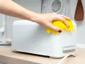 Eine Hand mit gelbem Tuch wischt über einen weißen Toaster. So einfach kann toaster reinigen sein.