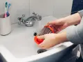 Hände reinigen einen staubigen Staubsaugerfilter unter fließendem Wasser im Waschbecken.