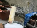 Eine Hand spritzt Wasser auf eine Malerrolle, um sie in einem Eimer mit Seifenwasser zu reinigen.