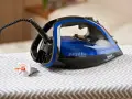 Ein Tefal Bügeleisen mit blauem Wassertank steht auf einem Bügelbrett. Der Stecker ist eingesteckt, aber das Bügeleisen scheint Wasser zu verlieren.
