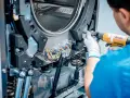 Techniker repariert die Schleudermechanik einer Waschmaschine mit einem Schrauber.