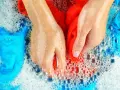 Hände waschen rote und blaue Sportsachen in schaumigem Wasser.