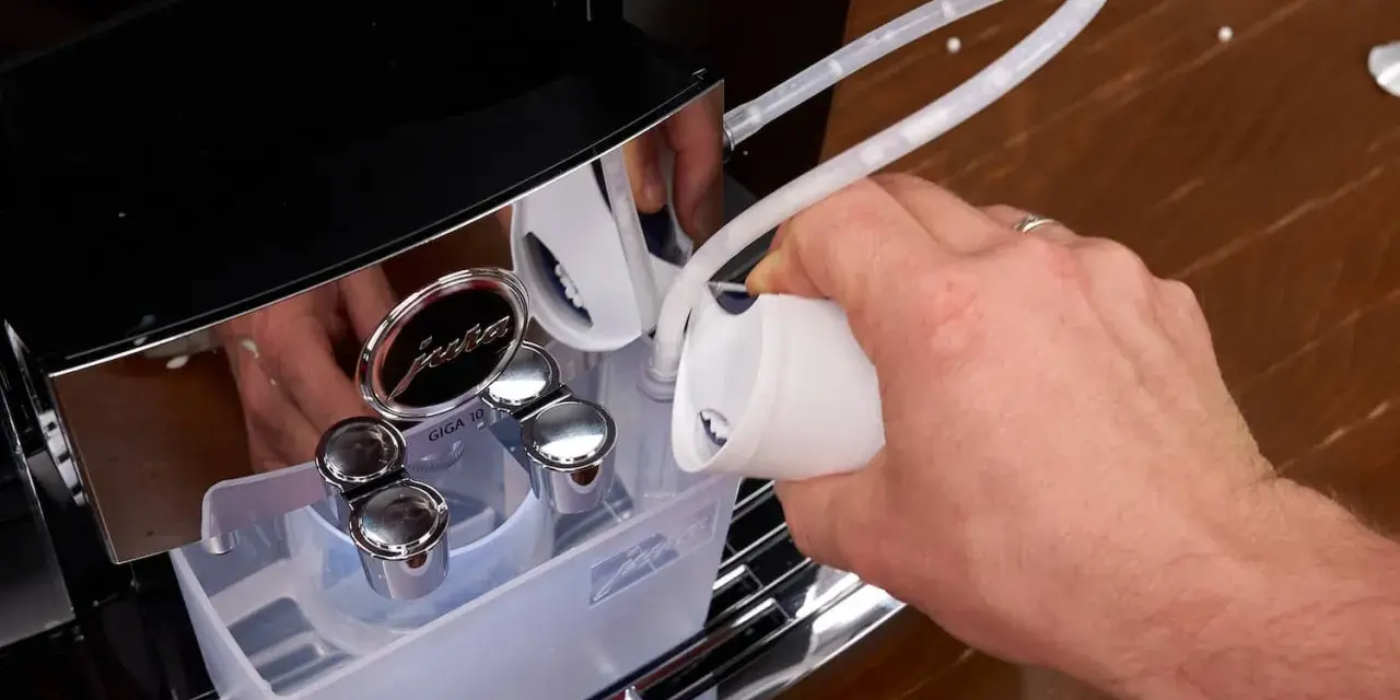 Hand gießt Flüssigkeit in einen Schlauch, um die Kaffeemaschine zu entkalken.