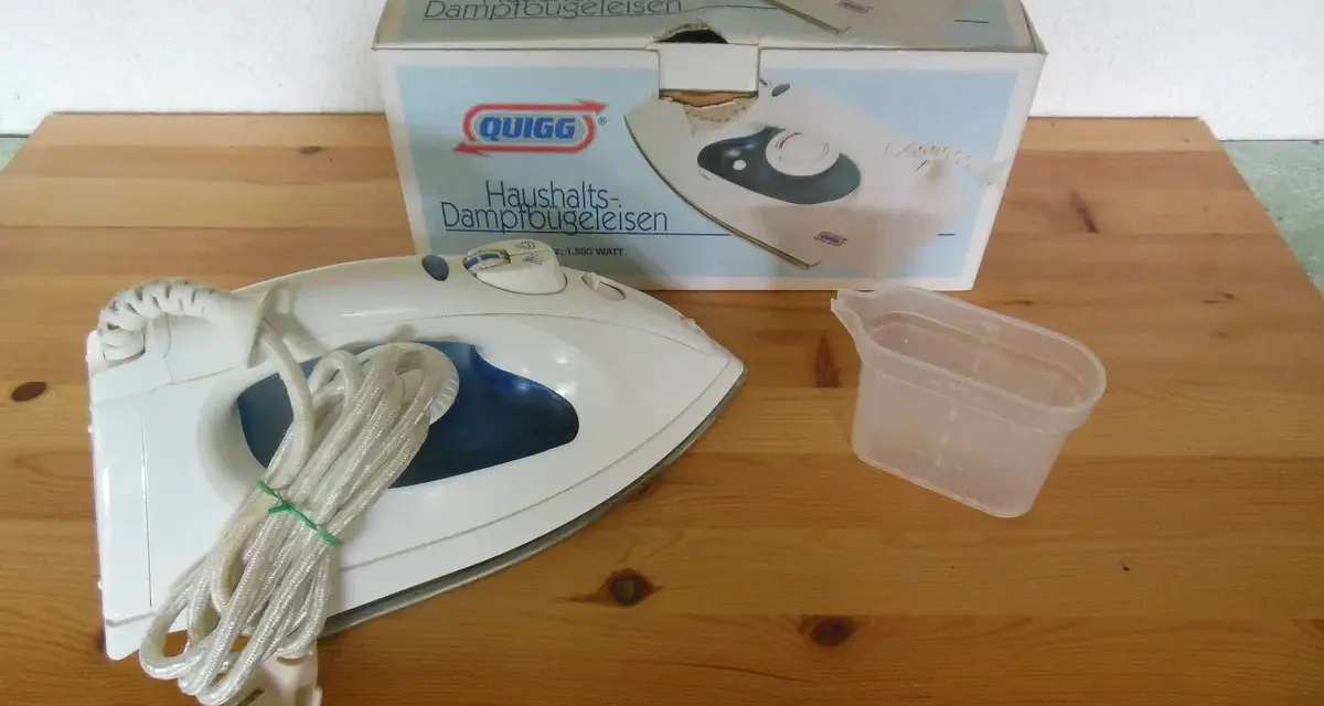 Ein Quigg Dampfbügeleisen mit Zubehör und Verpackung auf einem Holztisch.