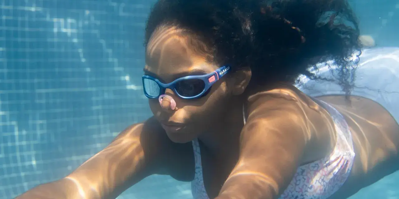 Ein Mädchen schwimmt unter Wasser. Ihre Schwimmbrille ist sauber und klar, damit sie alles sehen kann.
