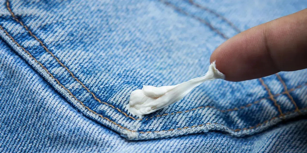 Finger versucht, Kaugummi aus Jeans zu entfernen. Der klebrige weiße Klumpen haftet an der blauen Denim-Oberfläche.