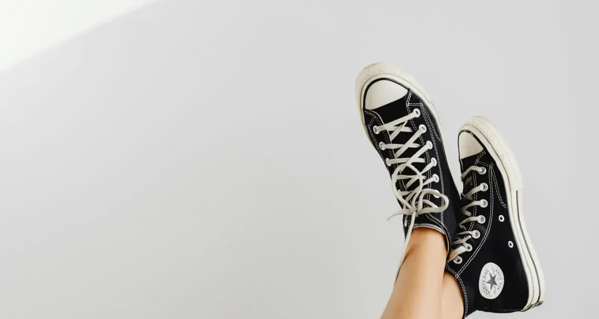Beine mit schwarzen Chucks, die in der Luft baumeln. Zeit, die Lieblingsschuhe zu waschen!