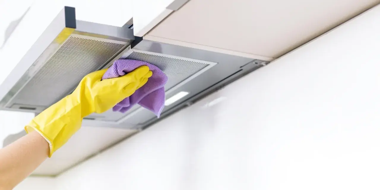 Gelbe Handschuhe wischen mit einem lila Tuch über die Dunstabzugshaube. Alu reinigen für strahlenden Glanz in der Küche.