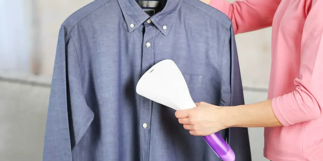 Dampfsteamer test: Eine Person glättet ein blaues Hemd mit einem Handdampfglätter.
