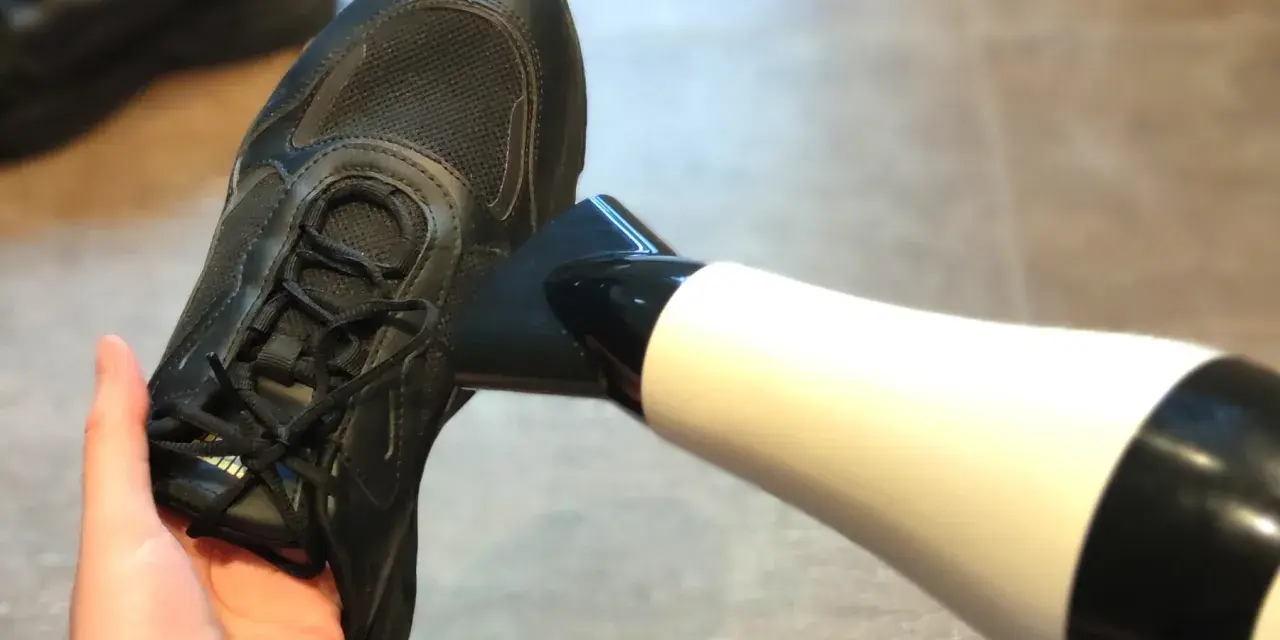 Schwarze Turnschuhe trocknen mit einem Föhn. Ein Paar nasse Schuhe wird mit einem Föhn getrocknet, um sie schnell wieder einsatzbereit zu machen.