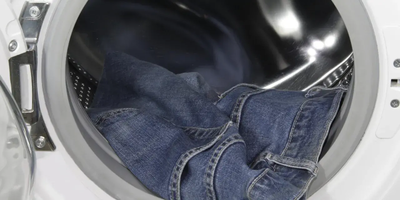 Eine blaue Jeans liegt in der Trommel einer Waschmaschine, bereit, um sie einlaufen zu lassen.