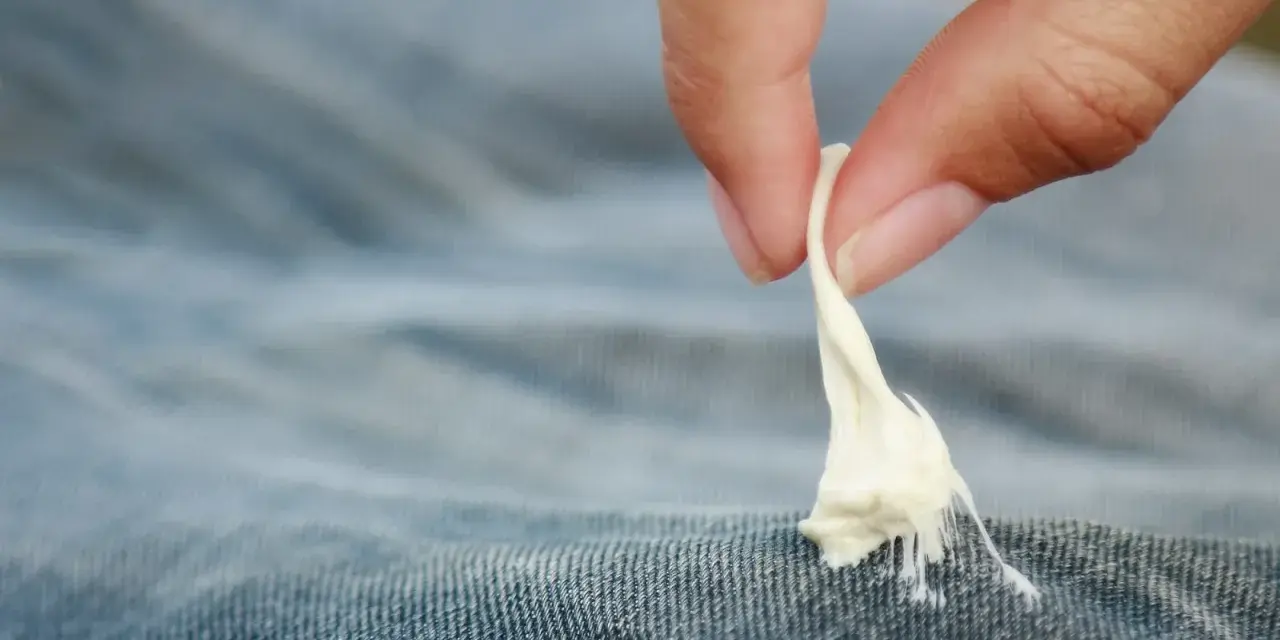 Finger zieht zähen Kaugummi aus Jeansstoff. Ein ärgerliches Malheur, das jeder kennt: Kaugummi aus Kleidung entfernen.