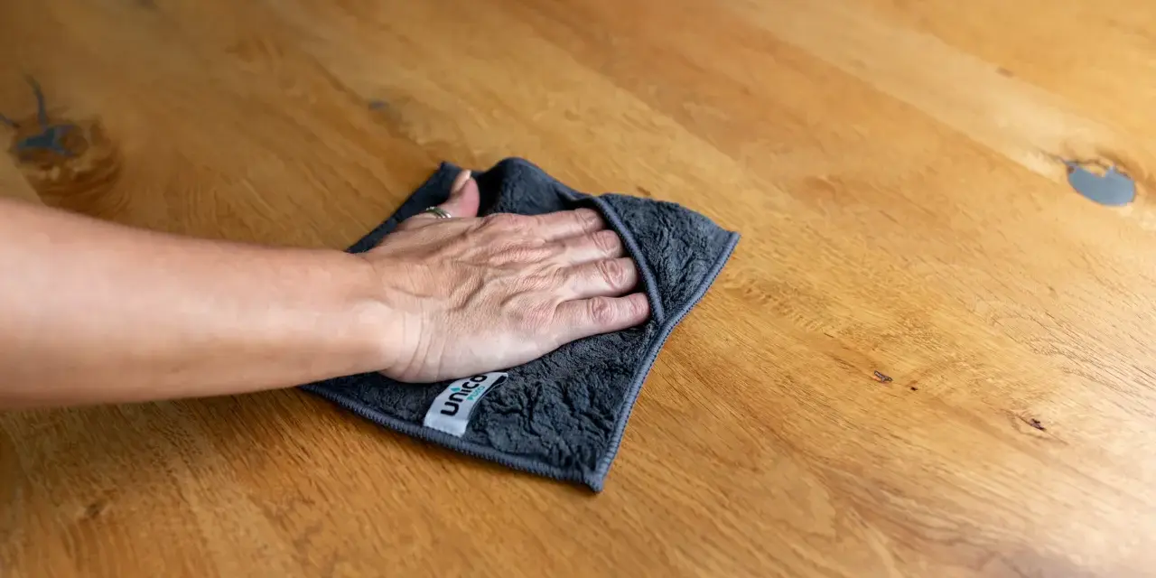 Hand wischt mit Tuch über Holzoberfläche, um Wasserflecken zu entfernen.