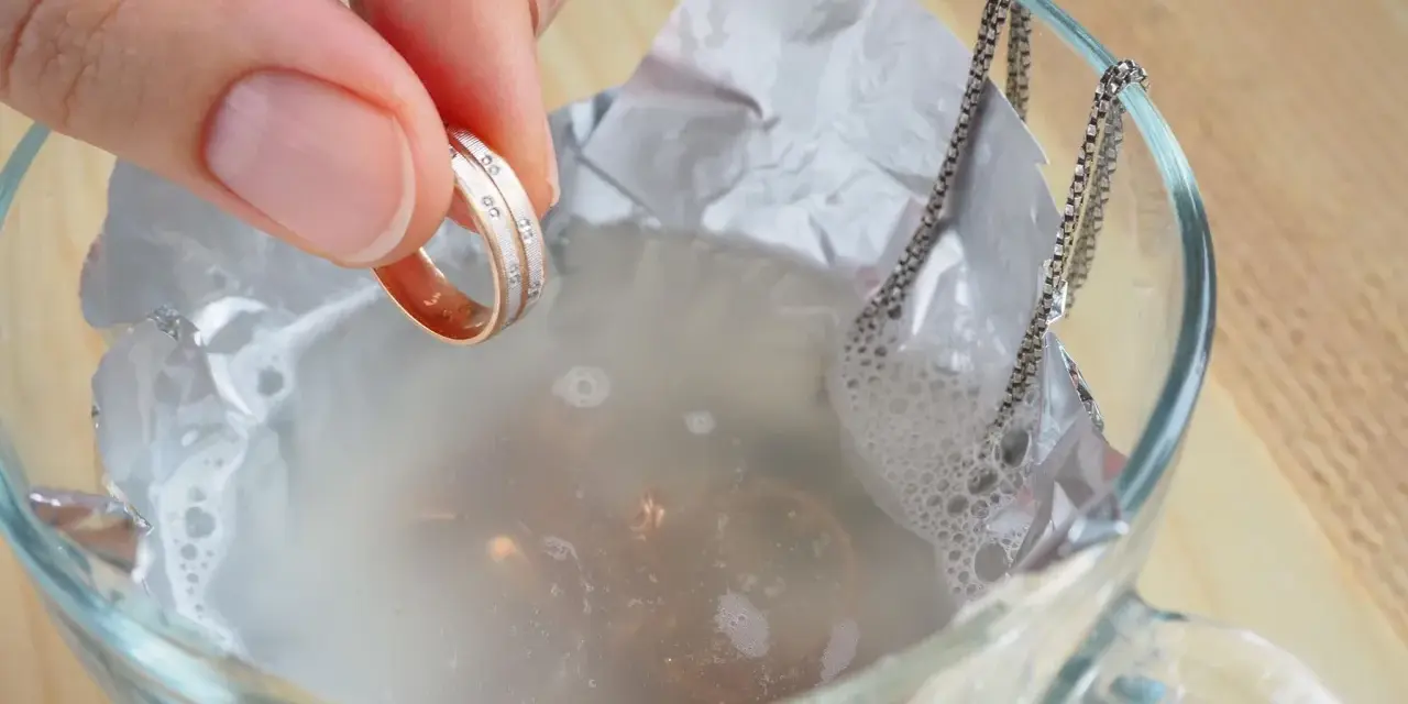 Ein Ring mit kleinen Steinen wird in eine Schüssel mit Wasser und Aluminiumfolie getaucht, um Schmuck zu reinigen.