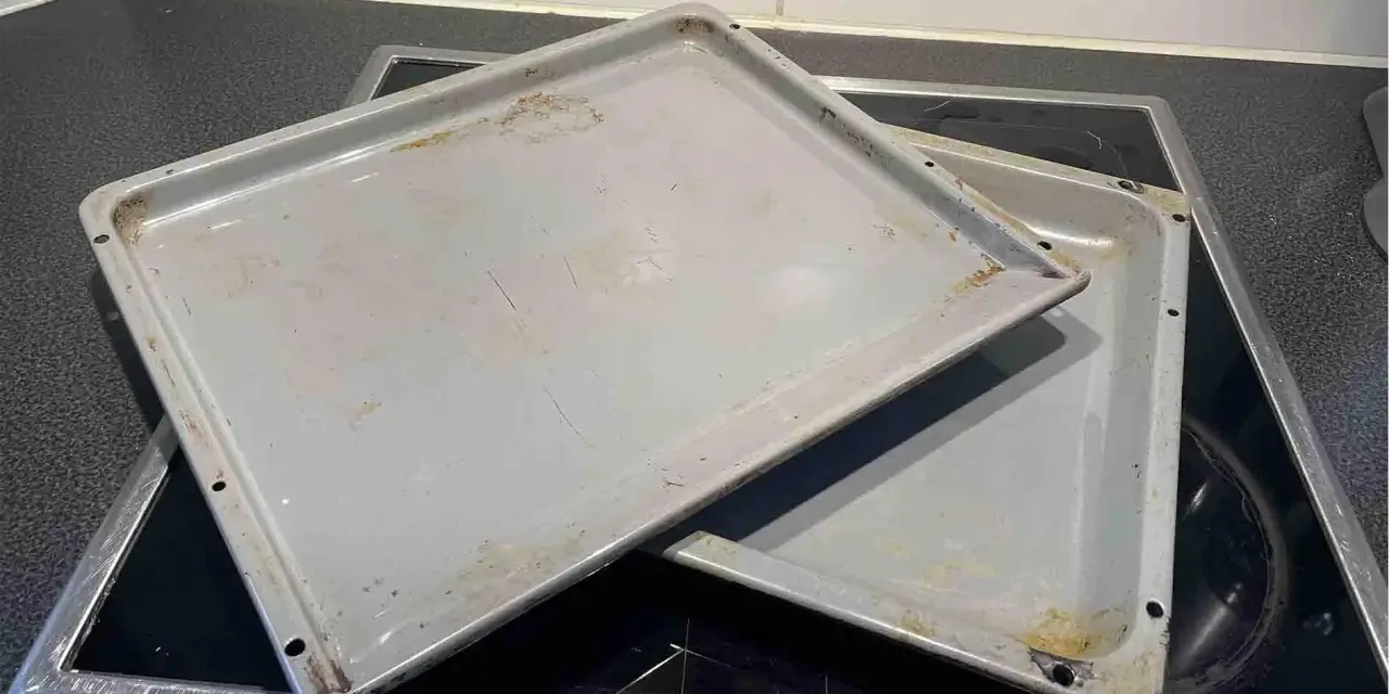 Zwei alte, graue Backbleche mit Gebrauchsspuren und Verfärbungen liegen übereinander auf einem Cerankochfeld. Zeit, das Backblech reinigen!