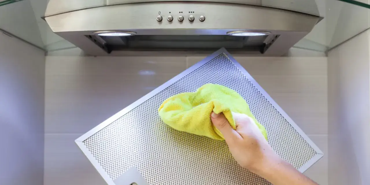 Hand reinigt Dunstabzugshaube mit gelbem Tuch.