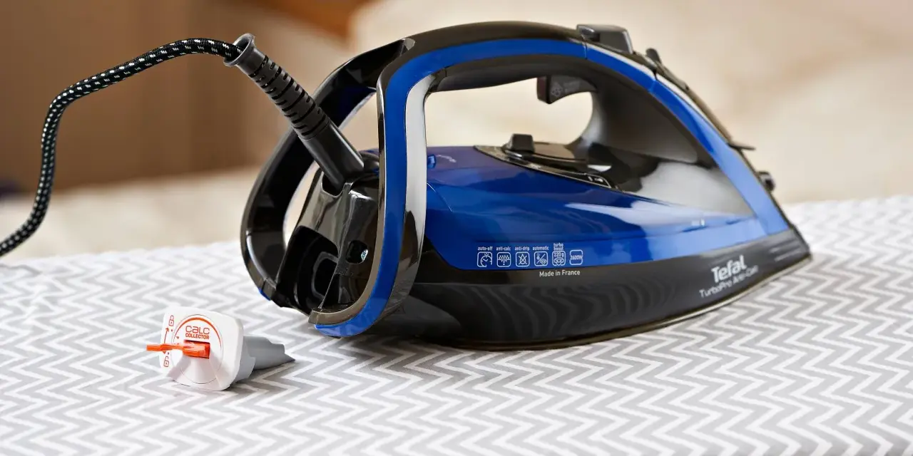Ein Tefal Bügeleisen mit blauem Wassertank steht auf einem Bügelbrett. Der Stecker ist eingesteckt, aber das Bügeleisen scheint Wasser zu verlieren.