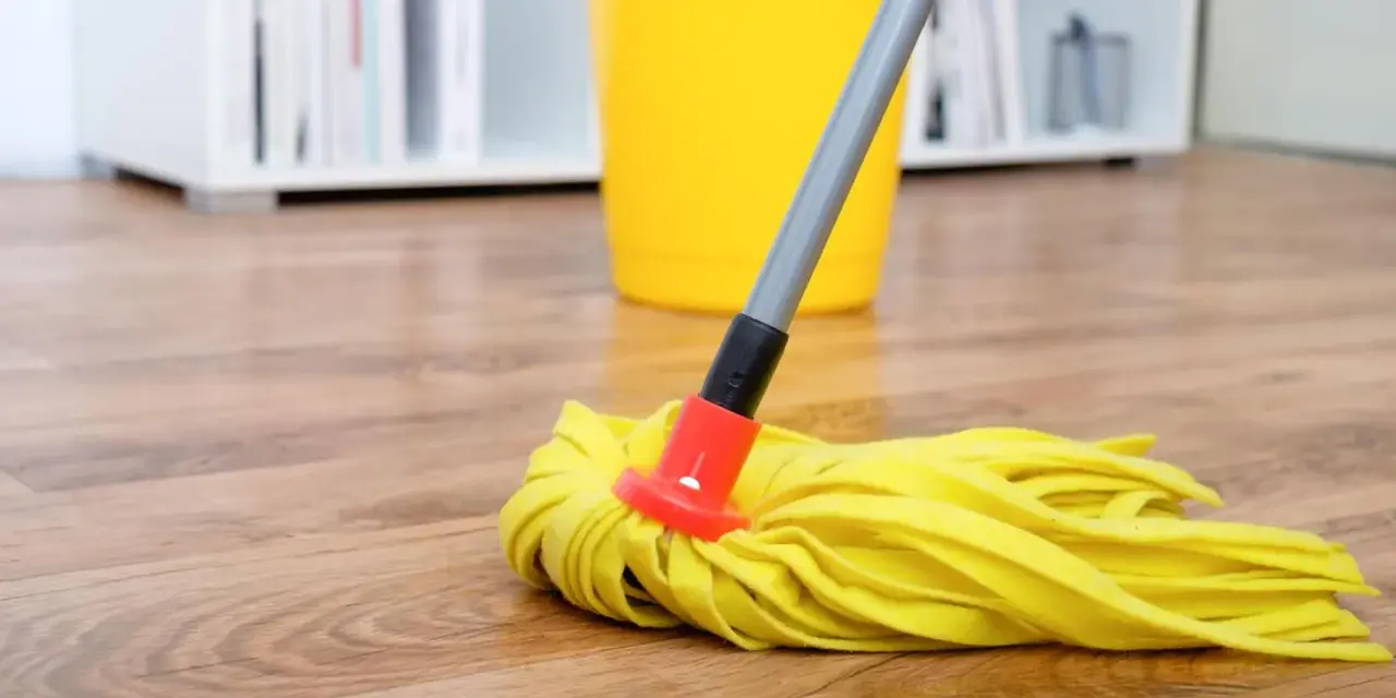 Gelber Wischmopp auf Laminatboden, bereit für die Reinigung mit Hausmitteln. Ein gelber Eimer steht im Hintergrund.