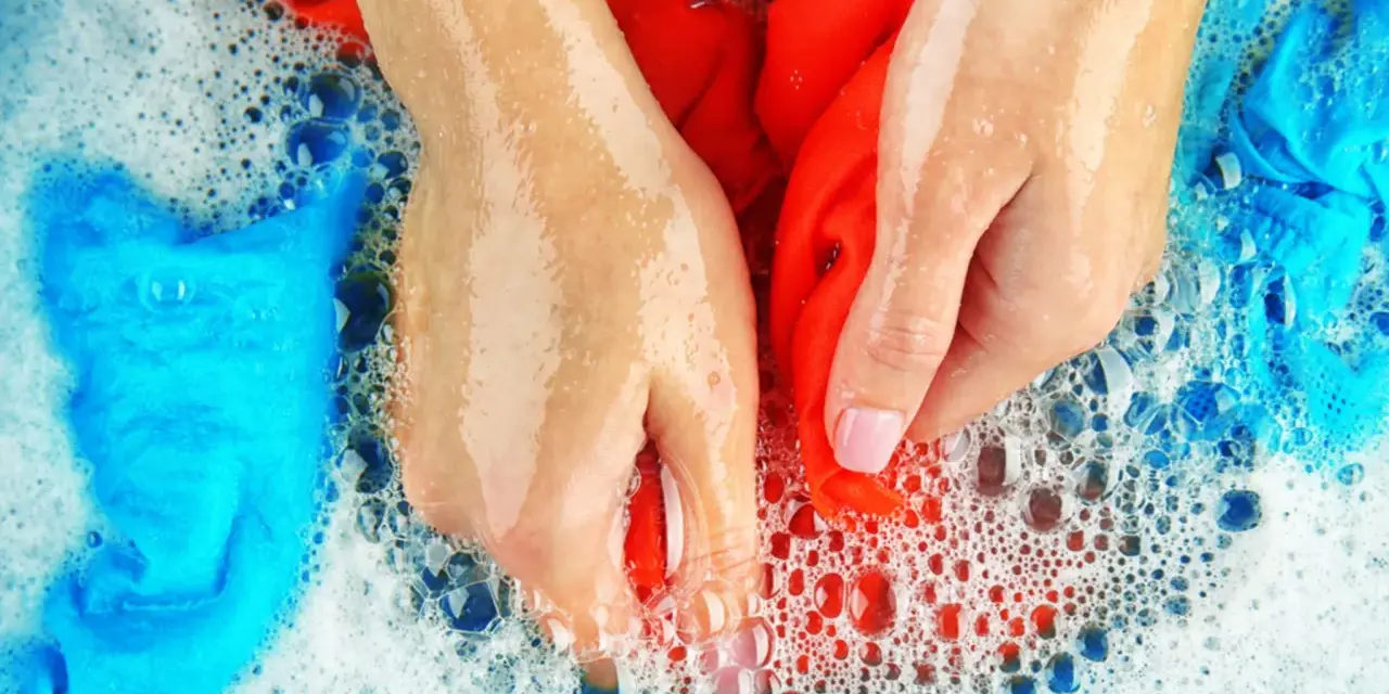 Hände waschen rote und blaue Sportsachen in schaumigem Wasser.