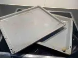 Zwei alte, graue Backbleche mit Gebrauchsspuren und Verfärbungen liegen übereinander auf einem Cerankochfeld. Zeit, das Backblech reinigen!