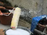 Eine Hand spritzt Wasser auf eine Malerrolle, um sie in einem Eimer mit Seifenwasser zu reinigen.