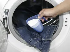 Eine Hand gibt Waschpulver in eine Waschmaschine, um Kettenfett aus Jeans zu entfernen.